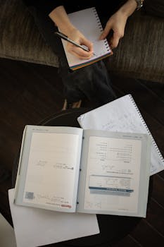 Person writing notes while studying from textbooks at home, photographed from above.