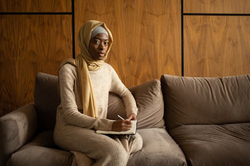 Free Serious black Muslim woman sitting on cozy sofa with notebook Stock Photo