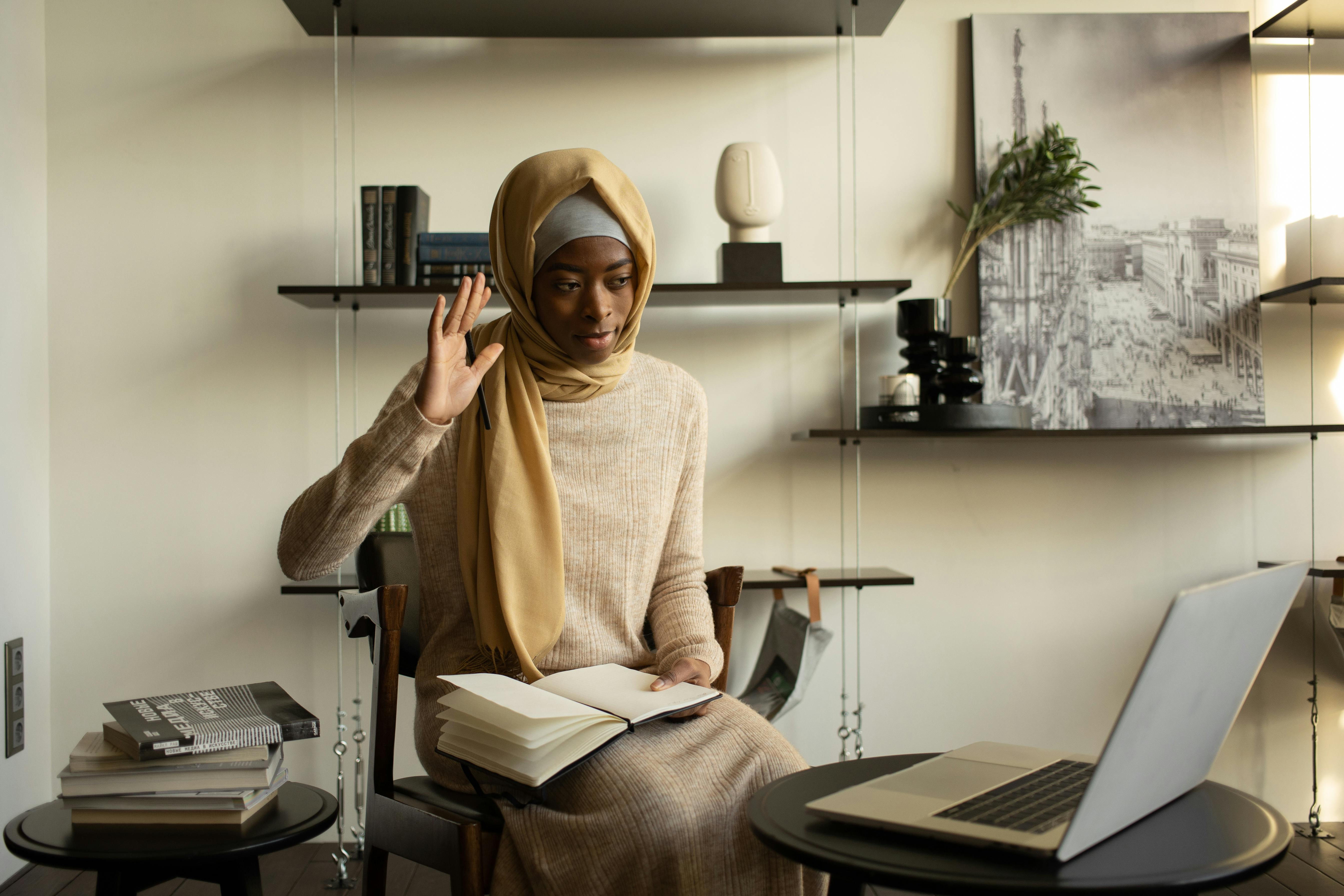 black muslim woman with notebook having video call via laptop