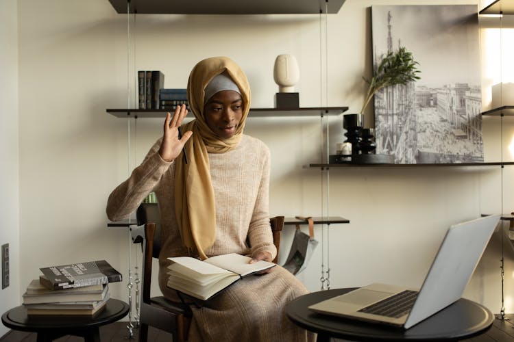 Black Muslim Woman With Notebook Having Video Call Via Laptop