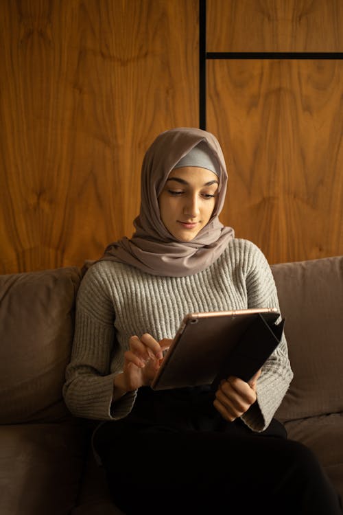 Free Positive Muslim woman using tablet on sofa Stock Photo