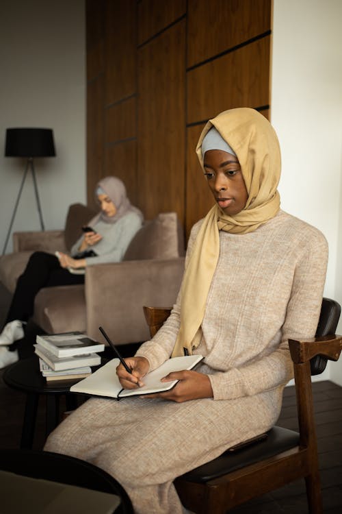 Free Black Muslim woman writing in notebook and studying at home Stock Photo