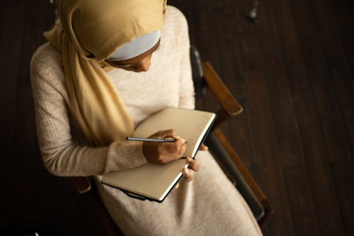 Free Crop black Muslim woman writing in planner Stock Photo