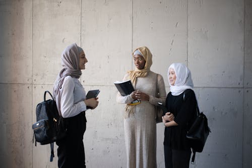 Free Cheerful diverse Muslim women with copybooks communicating in corridor of university Stock Photo