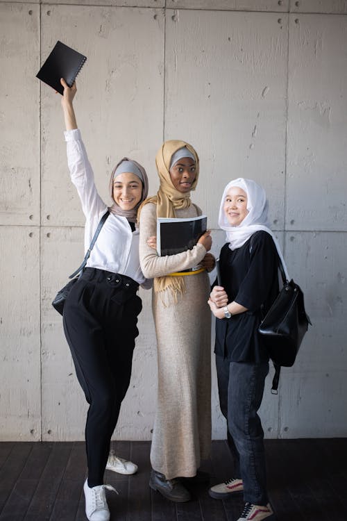 Happy multiethnic Muslim women in hijabs with workbooks in corridor of university