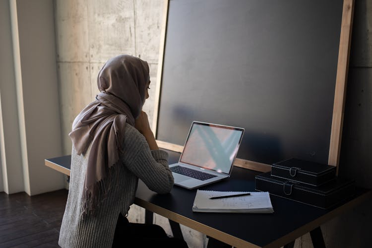 Serious Ethnic Woman In Hijab Browsing Laptop While Doing Homework