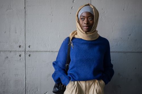 Free Content Muslim female student in traditional headscarf wearing blue sweater looking away while standing near wall with backpack in corridor of university Stock Photo