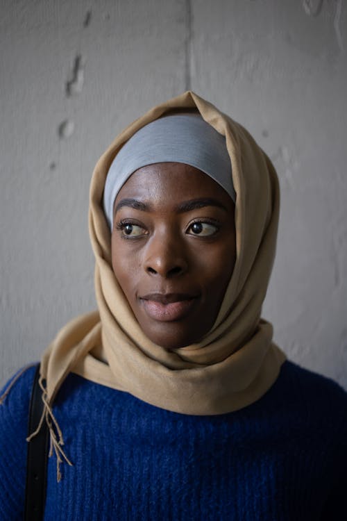Young Islamic African American female in national headscarf and hijab looking away near gray concrete wall