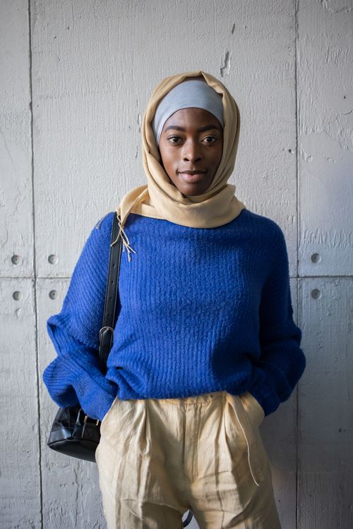 Free Confident Muslim black lady wearing casual outfit and hijab with backpack while standing near gray weathered wall with hands in pockets while looking at camera in light place Stock Photo