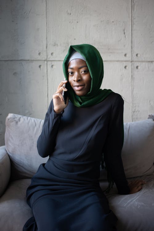 Женщина в зеленом хиджабе и черной рубашке с длинным рукавом сидит на диване