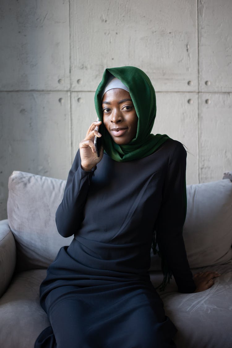 Black Muslim Lady In Hijab Talking On Phone On Couch