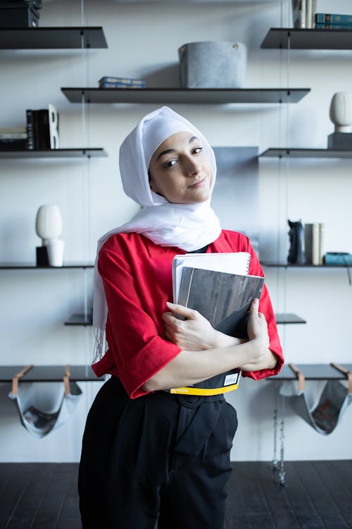 Muslim female with notebooks in apartment near shelves with decorations