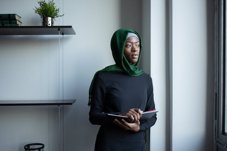 Thoughtful Black Muslim Lady In Hijab Standing With Notebook