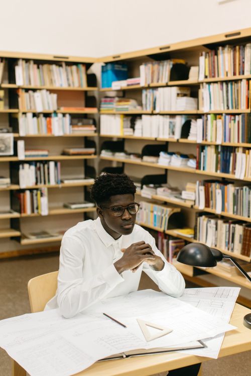 Free Young architect working on design plans in a library setting. Stock Photo