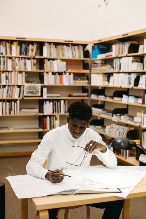 Free Architect deeply focused on blueprints in a library setting, planning a project with precision. Stock Photo