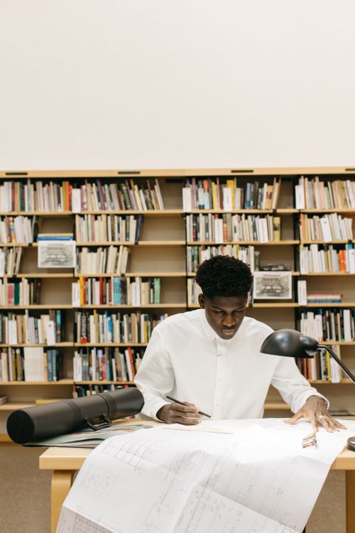 Free Architect working diligently on blueprints at a library table. Thoughtful design process in a scholarly setting. Stock Photo