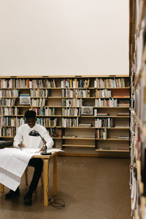 Free Focused architect reviewing blueprints in a library setting, surrounded by bookshelves. Stock Photo