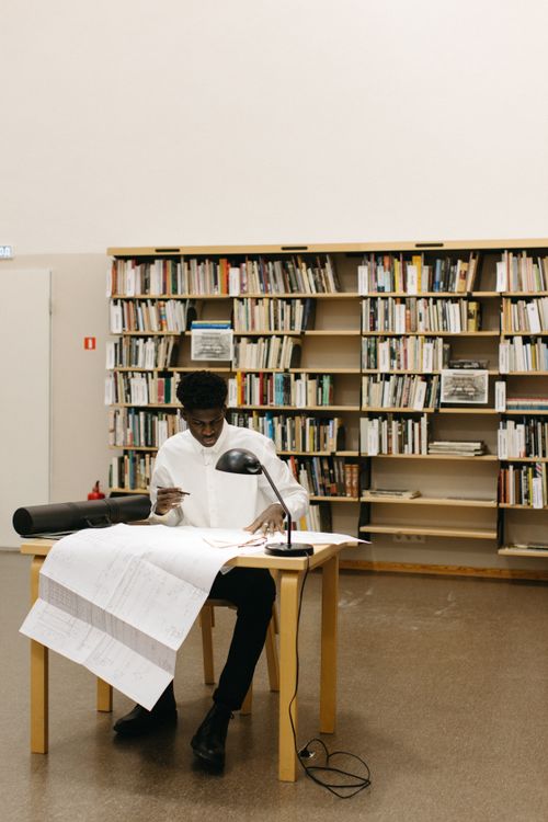 Free Architect working at a desk with blueprints in a library setting, focused on designs. Stock Photo