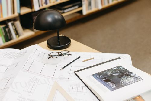 Free A workspace with architectural blueprints, glasses, and a desk lamp on display. Stock Photo