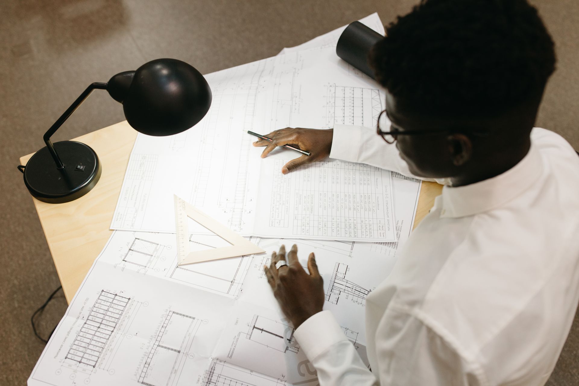 Top view of architect with afro hair working on blueprints at desk inside an office.
