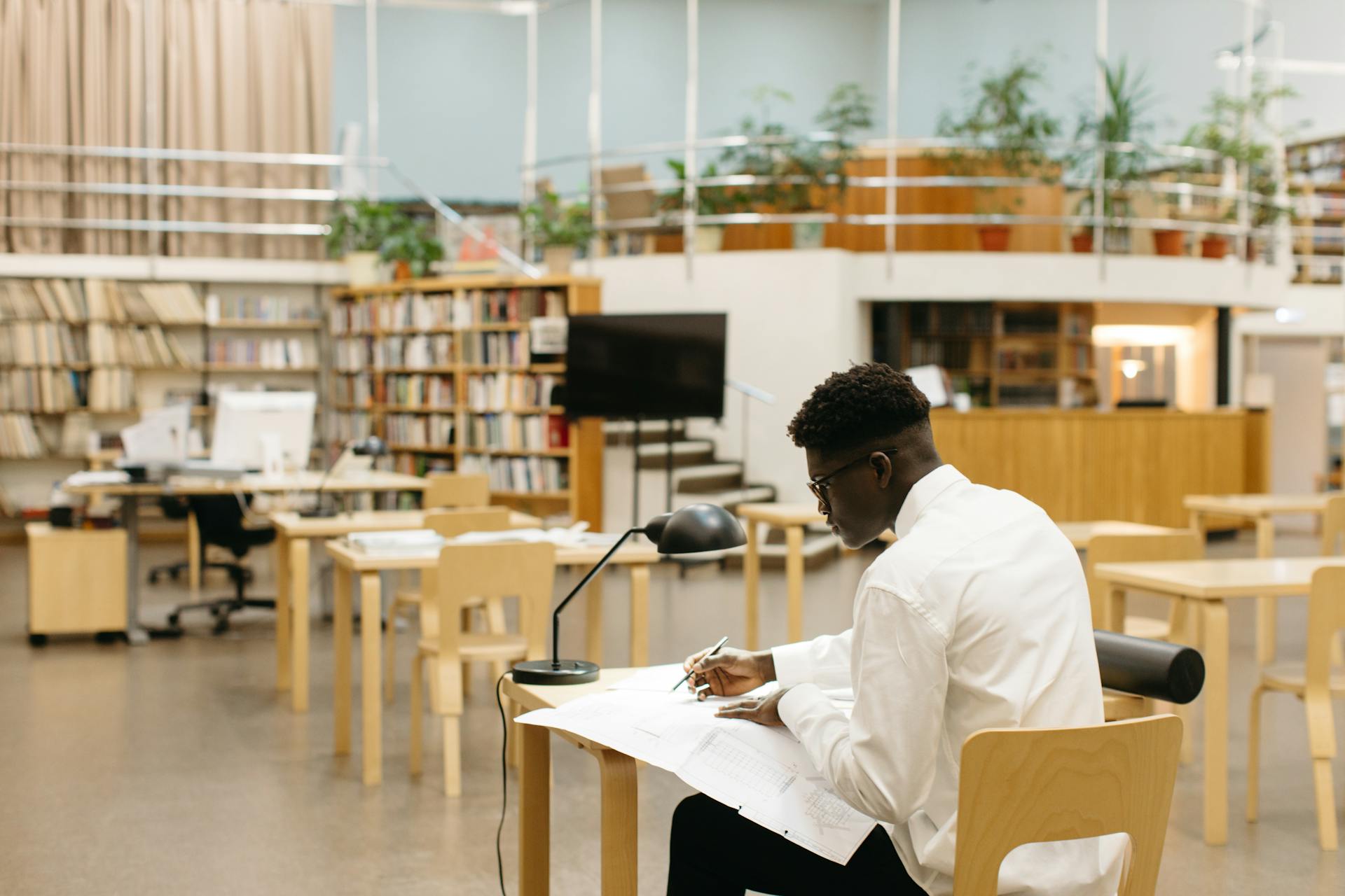 Architect focused on drafting plans in a modern library workspace.