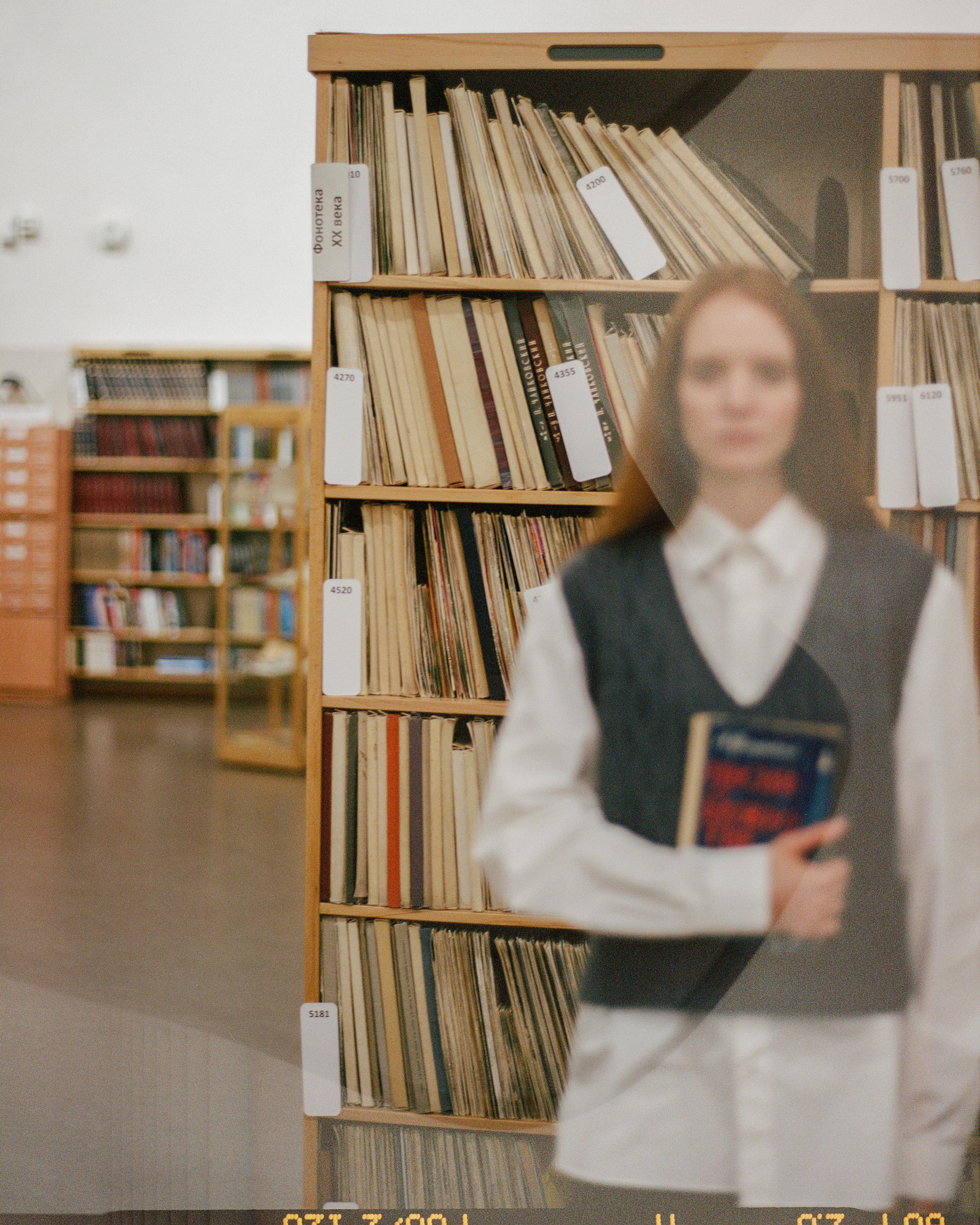 Free Blurred image of a woman in a library holding a book, surrounded by shelves. Stock Photo