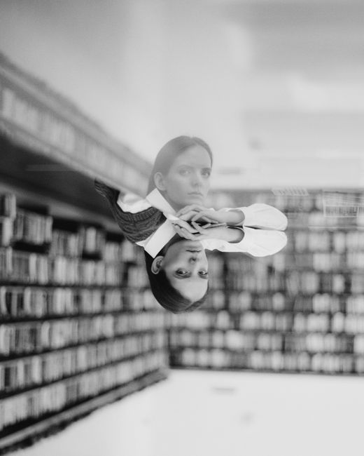 Contemplative woman reflected in library scene, conceptual B&W image.