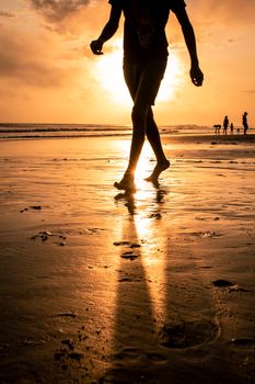 A silhouette of a man strolling on a sandy beach during a vibrant sunset, creating a serene coastal scene.