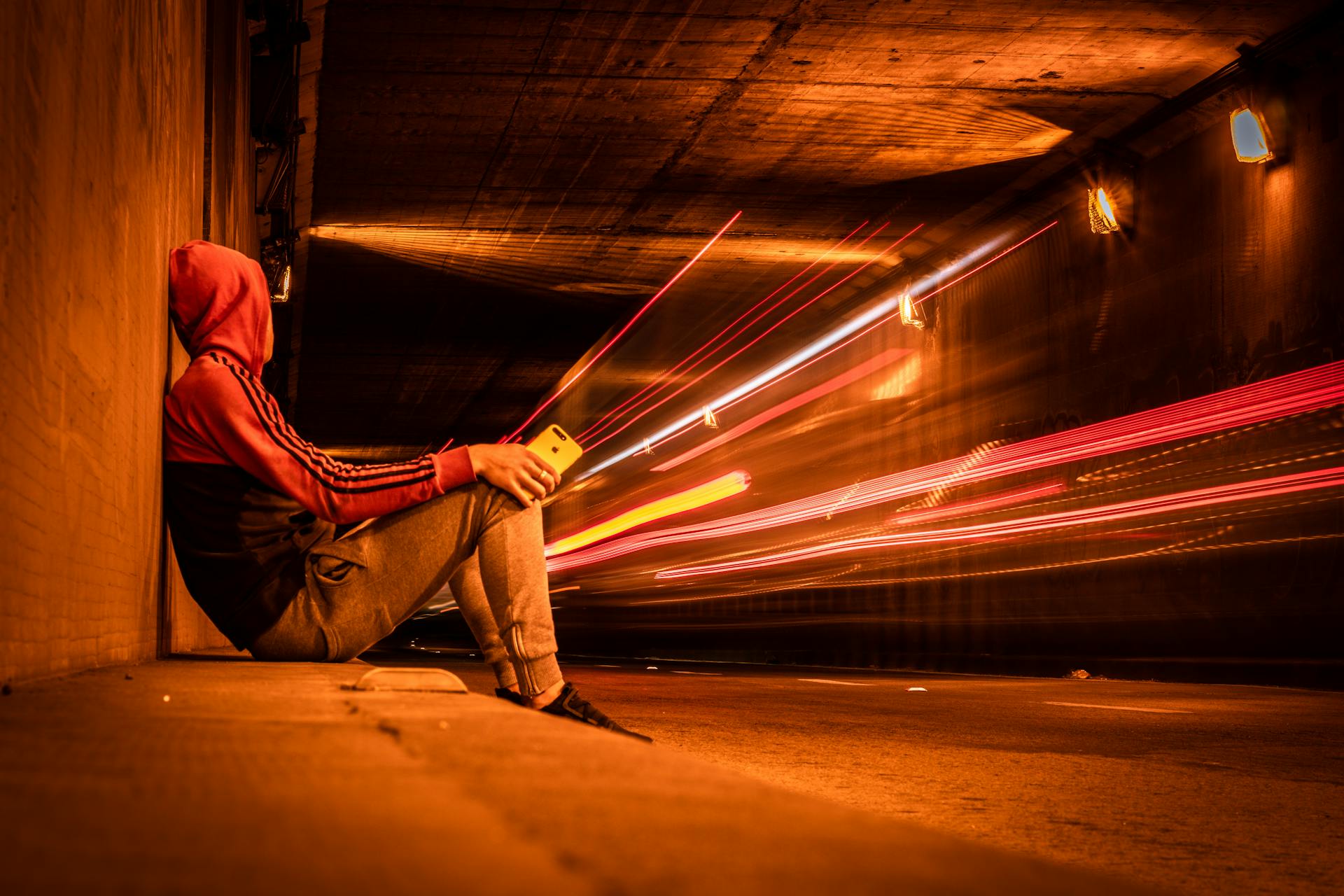 Man in hoodie sitting in Montevideo tunnel with dynamic light trails and moody ambiance.