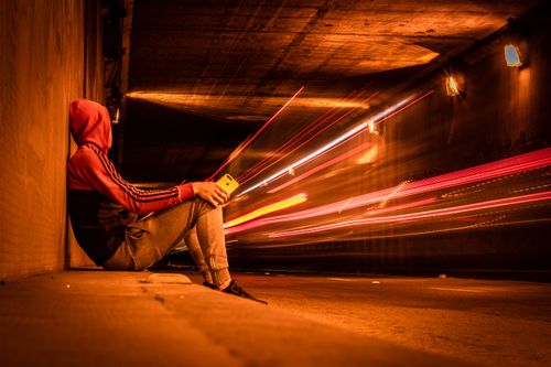 Free Man in hoodie sitting in Montevideo tunnel with dynamic light trails and moody ambiance. Stock Photo