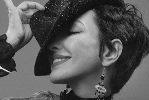 Chic monochrome portrait of a woman smiling while tipping her fedora hat with stylish earrings.