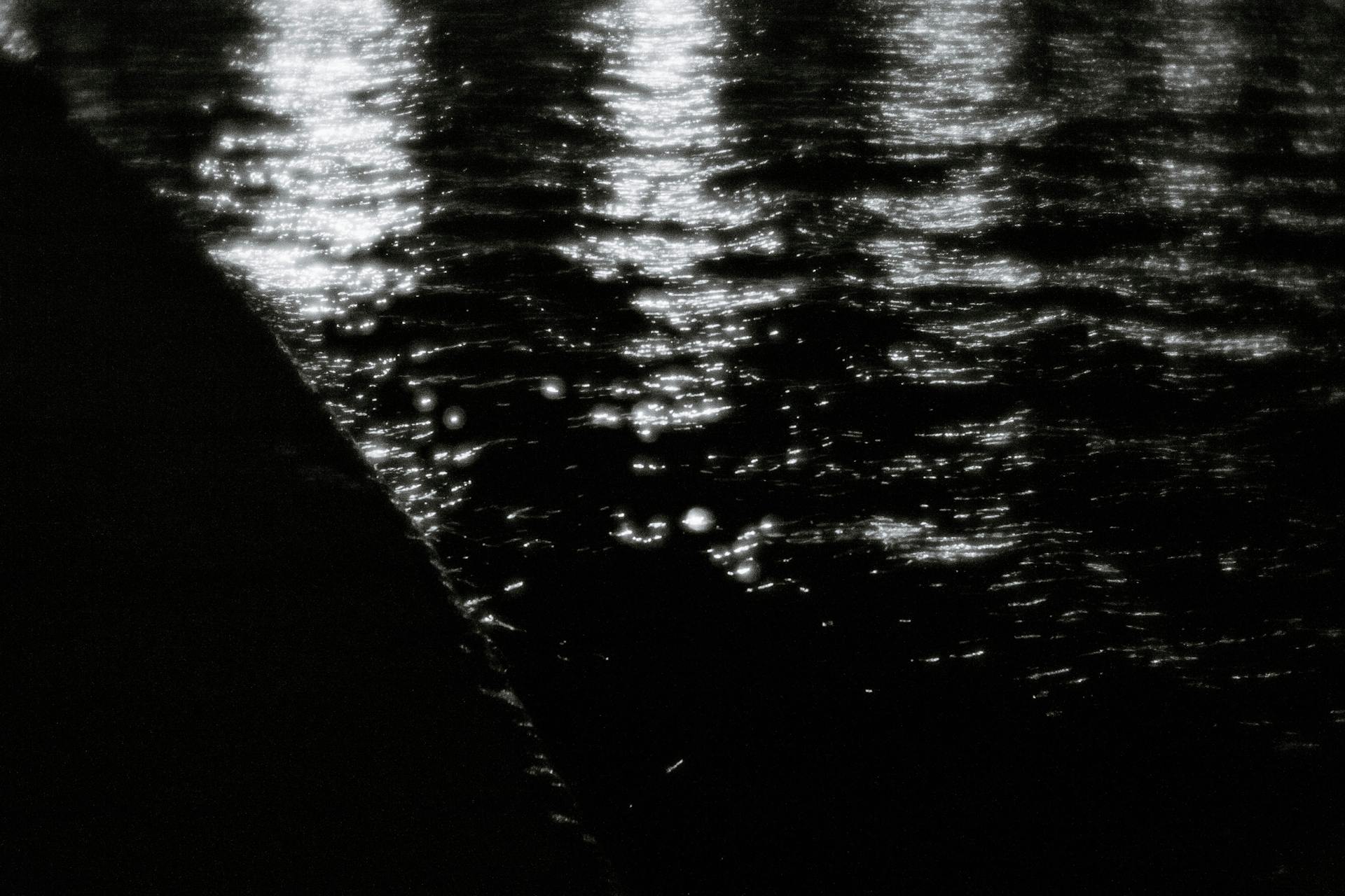 A mesmerizing abstract black and white water reflection at night, capturing shimmering light patterns.