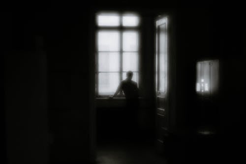 Monochrome Shot of Person Standing near the Window