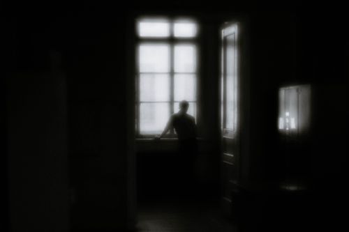 Free A moody black-and-white silhouette of a person standing by a window indoors. Stock Photo