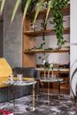 Modern apartment interior details with  marble tables placed near comfortable sofa and wooden shelves decorated with fresh plants