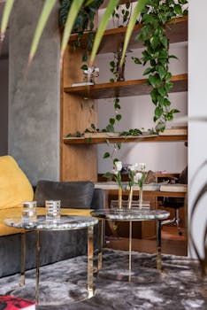 Modern apartment interior details with  marble tables placed near comfortable sofa and wooden shelves decorated with fresh plants