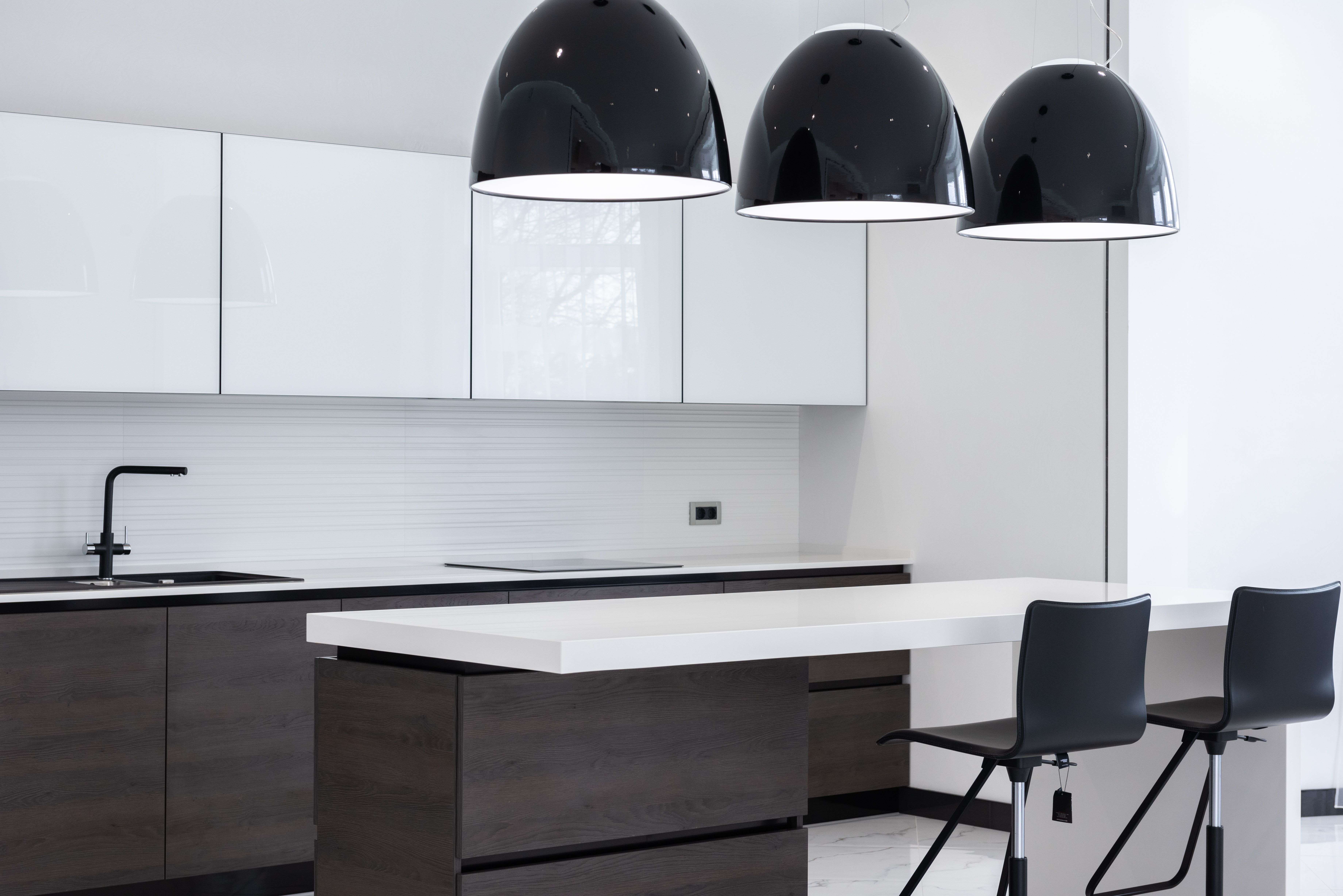 Interior of modern kitchen with minimalist furniture and creative lamps hanging above counter and bar chairs