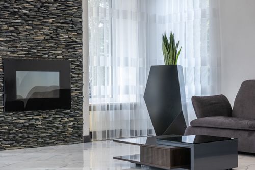 Free Electric fireplace on creative stone wall in spacious modern living room with cozy sofa and exotic potted plant Stock Photo