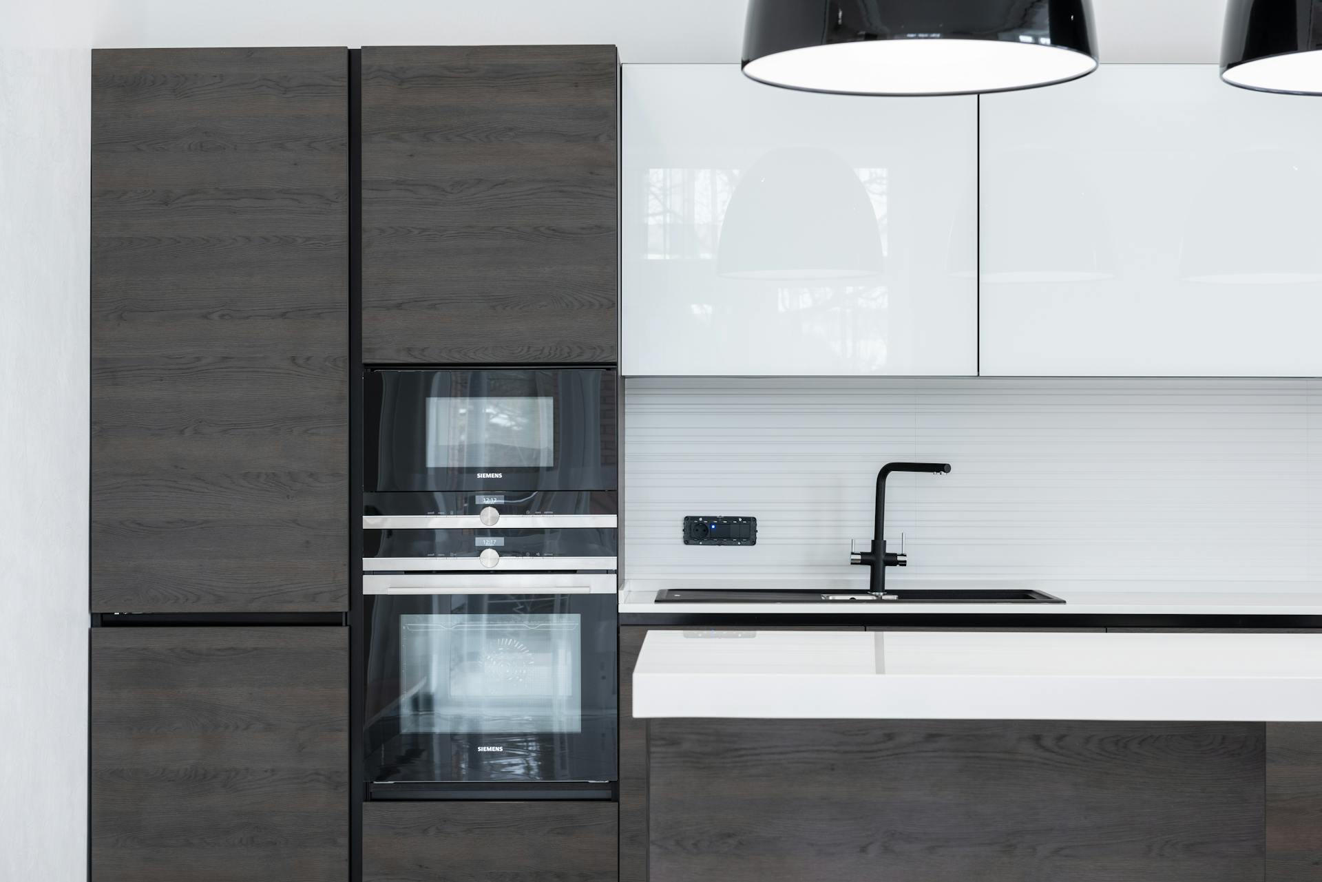 Interior detail of modern kitchen with minimalist furniture contemporary appliances decorated with lamps hanging over counter