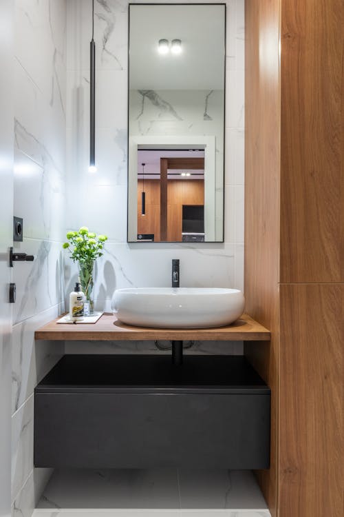 White ceramic sink and mirror in modern bathroom with wooden furniture and marble walls