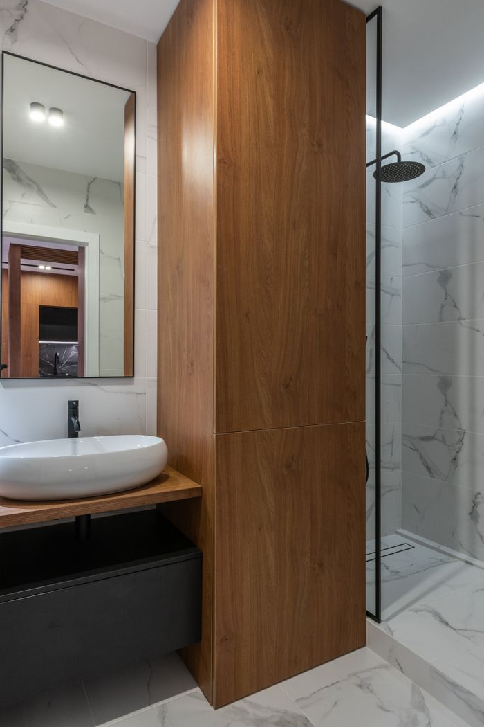 Fertiges Bad mit Marmoroptik, Holzschrank und schwarzer Regendusche