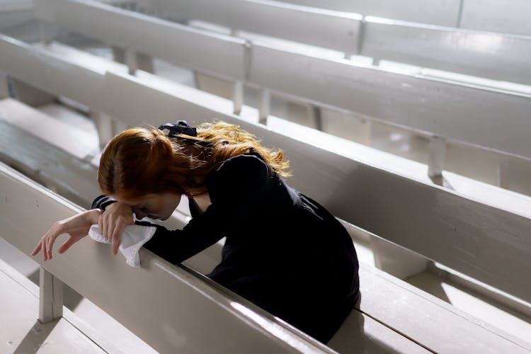 A Woman In Black Long Sleeve Shirt Sitting Alone On Wooden Pew