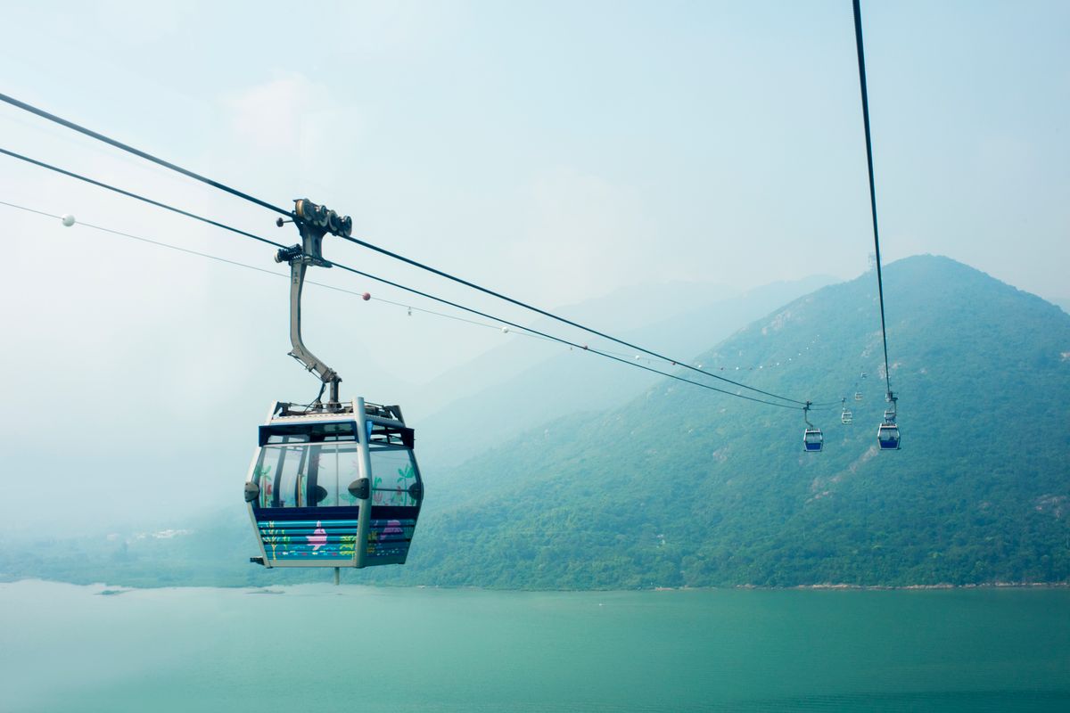 Cable car gondola crossing above forested mountains and lake water