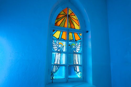 Free A stunning arched church window featuring colorful stained glass with angel artwork, creating vibrant light reflections. Stock Photo