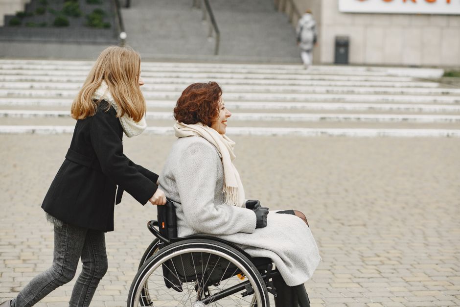 A young girl pushing a woman in a wheelchair outside on a stone pavement.