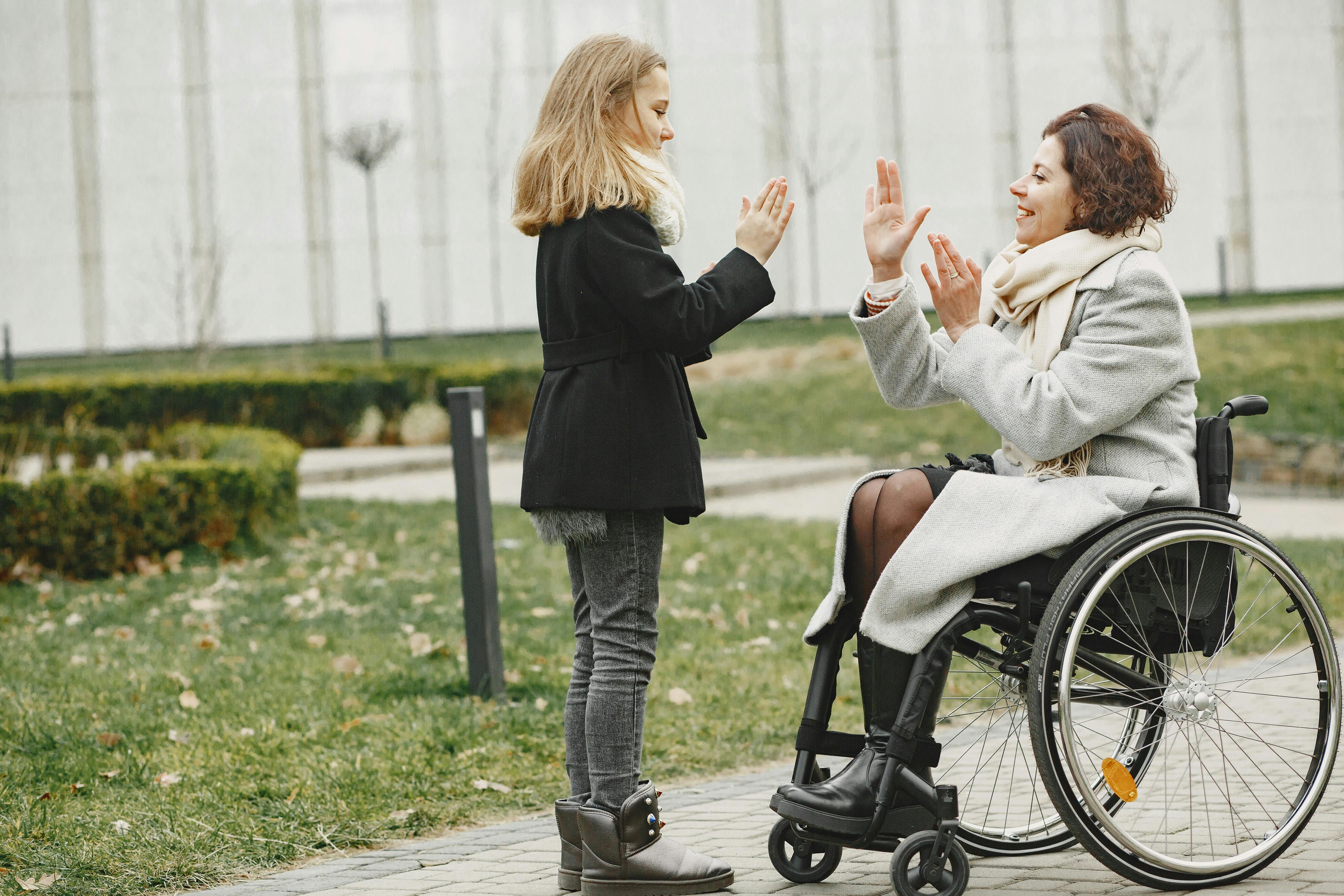 Happy child and woman in wheelchair sharing a joyful moment outdoors.