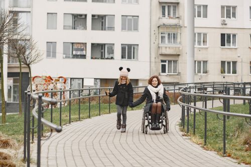 Free A heartwarming scene of a woman in a wheelchair holding hands with a girl outdoors on a pathway. Stock Photo