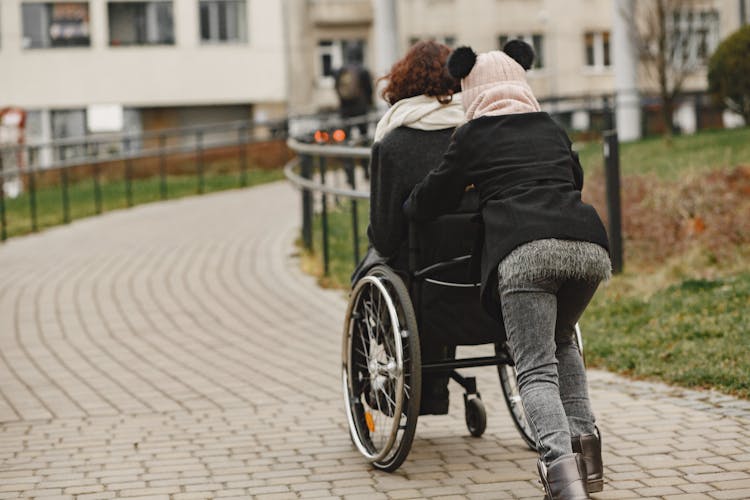 A Girl Pushing A Woman In A Wheelchair