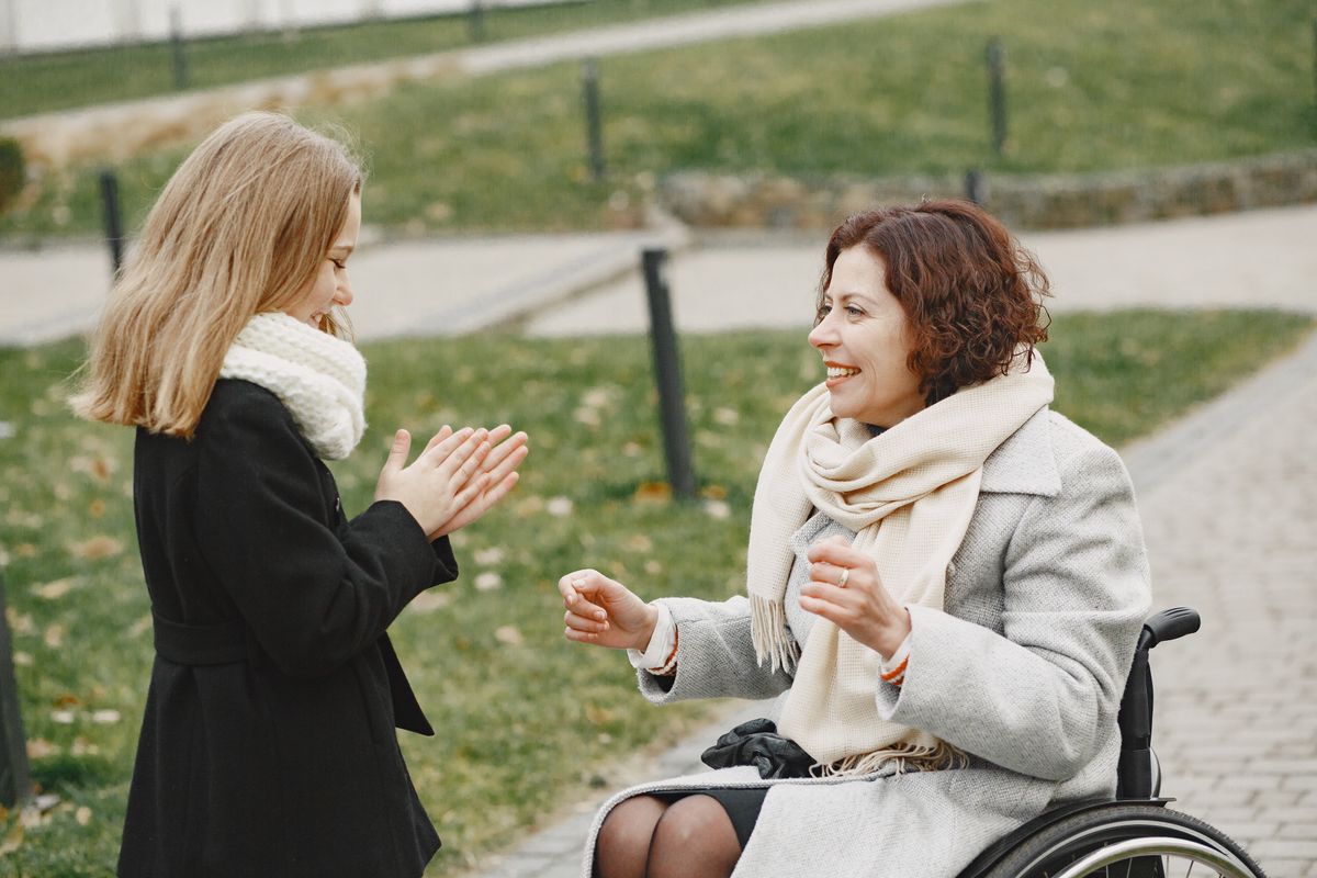 A woman in a wheelchair laughing and playing outdoors with a young girl