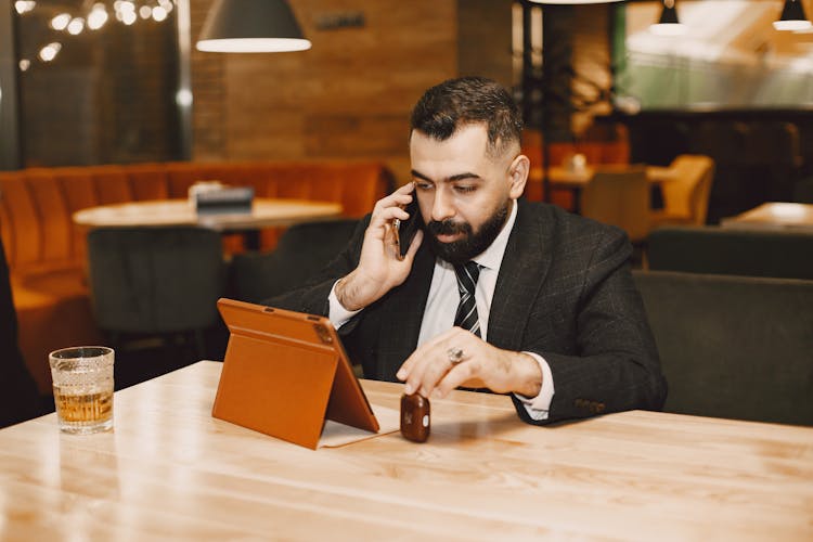 A Man Talking On The Cellphone While Looking At An Ipad In A Restaurant